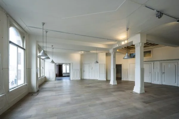 Lichte, leegstaande ruimte aan de De Ruijterkade met houten vloer, witte muren en grote ramen.